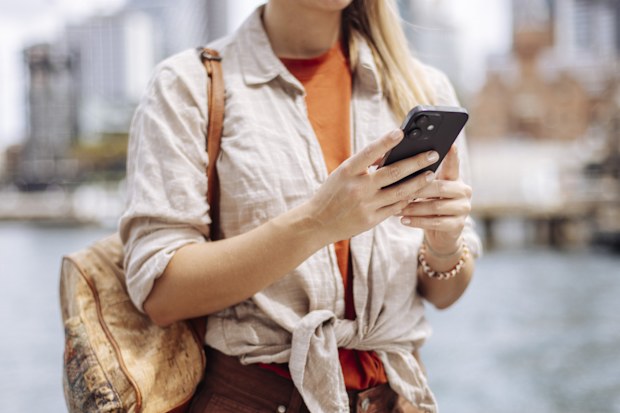 Close up of an unrecognizable tourist standing at waterfront and using cellphone for navigation