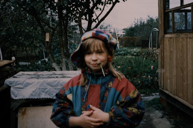 Little girl wearing warm clothing is standing in the backyard and looking at camera. Vintage photo