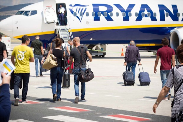 Passengers walking with carry-on luggage toward a Ryanair plane. 