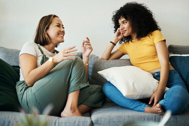 Women, friends talk and conversation in a home with gossip, discussion and happy in a living room. Couch, smile and female person on a sofa with communication together in a house lounge with speaking
