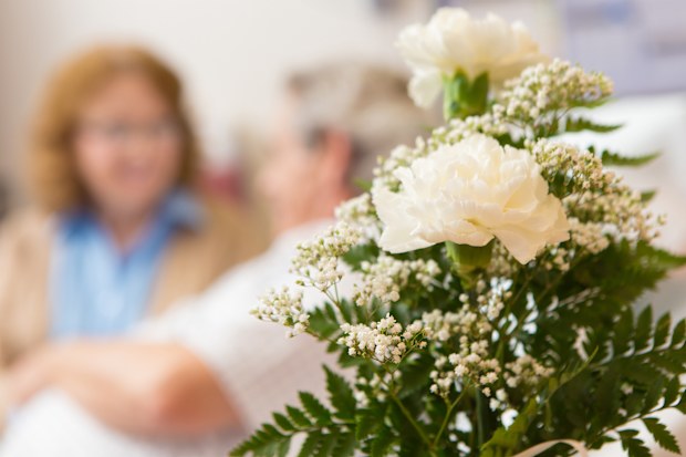 Closeup of flowers with senior couple in hospital patient room.