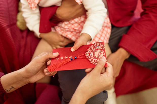 Close up of a mother giving an ornate red envelope to little girl as a good fortune tradition for Chinese New Year