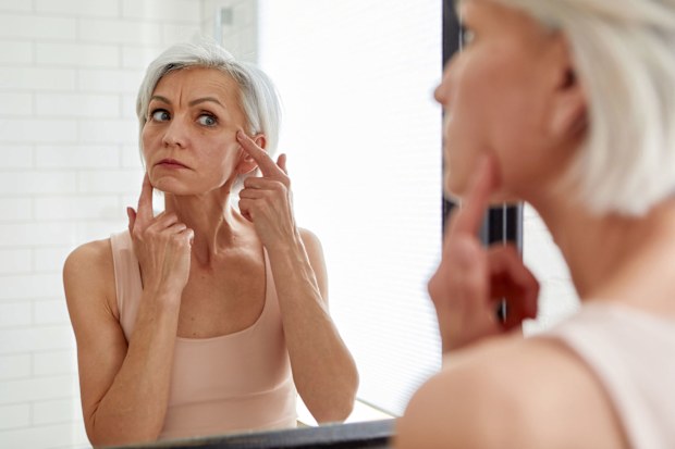 Elderly woman examining face in mirror - stock photo