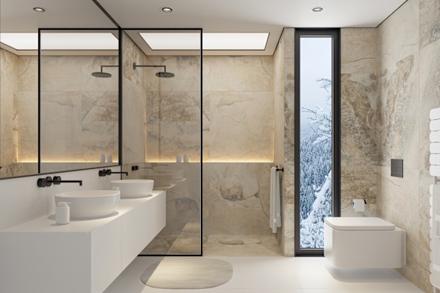 A sleek and sophisticated modern bathroom featuring large limestone or travertine tiles on the walls and floors. The space includes two elegant sinks, a minimalist toilet, and a spacious shower with a contemporary shower head. The expansive mirror enhances the sense of openness, while the natural stone elements provide a serene and luxurious atmosphere. This image is perfect for interior design projects, bathroom renovations, or showcasing high-end bathroom furnishings and fixtures.