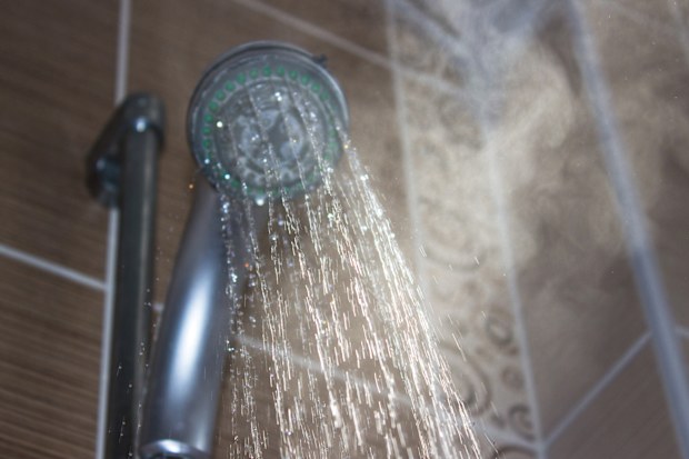 Low angle view of flowing shower head in the bathroom. Horizontal composition. Image taken indoors and developed from Raw format. Focus on water. Shower head and other background are blurred.