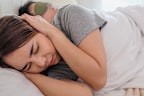 Portrait of Asian young couple lying down on bed covered with blanket, Men wearing sleeping mask and and sleep, Women covering her ears with hands while man snoring in bedroom at home, Sleep Apnea and Relationship Difficulties