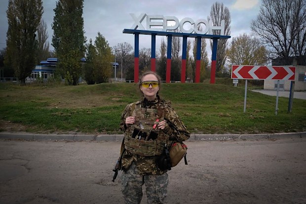 A Ukrainian female soldier poses for a photo against a Kherson sign in the background, in Kherson, Ukraine, Friday, November 11, 2022 