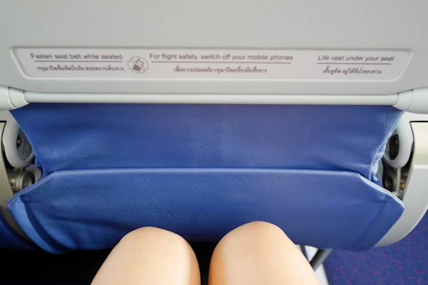 Woman's legs sitting in a plane with warning sign on the front seat legroom