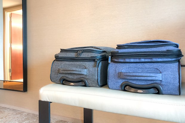 Two pieces of rolling, carry-on luggage sit together on a leather hotel bench as they wait to be opened and unpacked. They are the same size and brand but different colors.