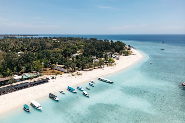 Boats anchored on white sand beach with lush green trees, surrounded by the clear turquoise ocean in Indonesia