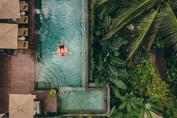 Aerial view of luxury resort with man on inflatable ring in pool. Top view of hotel surrounded with trees.