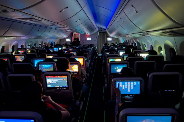 ISTANBUL AIRPORT, TURKEY, 30th JANUARY 2024: CLOSE UP: Tourists aboard a commercial airplane use their in-flight entertainment screens to watch flight details, movies and play games in the dark.