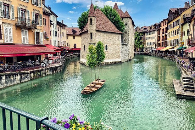 Annecy, France - June 13, 2020. View of the historic district of Annecy Old town. in the foreground, the river Thiou on which a decorative boat is visible. in the background, the picturesque old buildings of Annecy