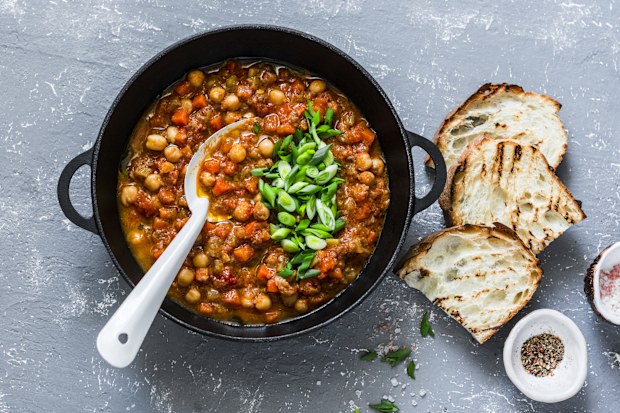 Vegetarian mushrooms chickpea stew in a iron pan and rustic grilled bread on a gray background, top view. Healthy vegetarian food concept. Vegetarian chili