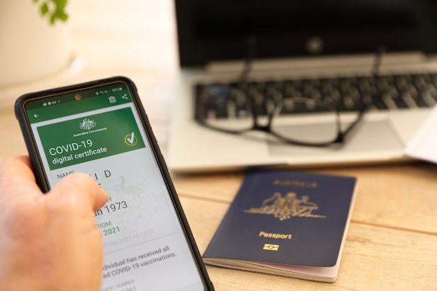 The official Australian government digital proof of covid-19 vaccination certificate on a mobile phone device. Passport blurred in background and laptop.