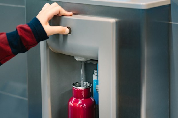 Hand of a traveler pressed the button of drinking water filling station at the Airport