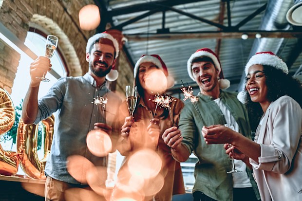 Young creative team with sparklers and Santa hats celebrating the holidays in a modern office. 