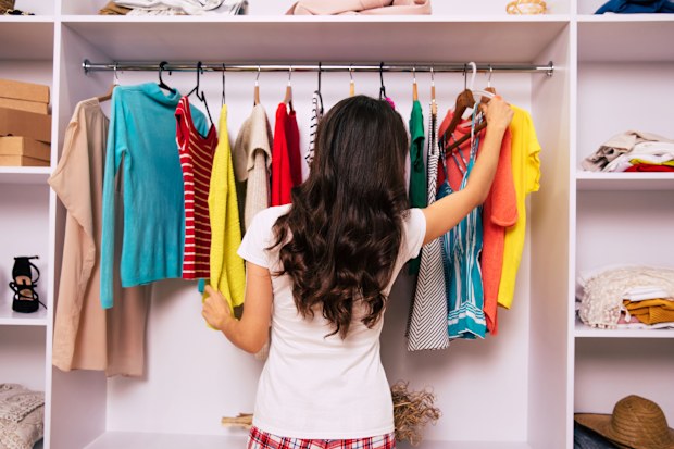 Close-up photo of a nice woman in pajamas, who is standing with her back to the camera, trying to choose an item of clothing to wear from clothes in her wardrobe.
