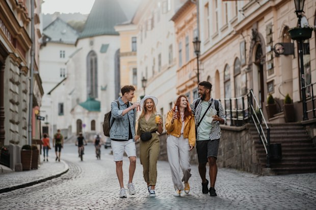 A front view of group of happy young people with drinks outdoors on street on town trip, laughing.
