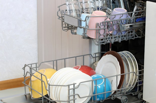 Open dishwasher with clean colorful dishes and mugs inside, ready for unloading after washing cycle