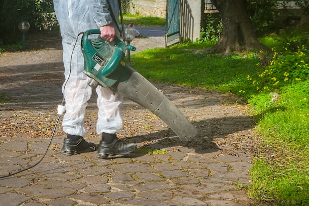 Man wearing a white suit uses a leaf blower in a garden, in a sunny day