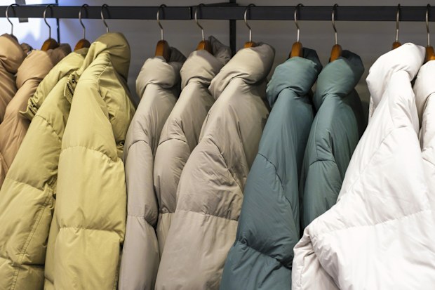Multicolored winter down jackets hanging on hangers in the store close up, side view.