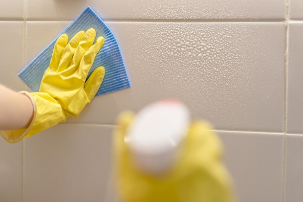 woman washes ceramic tiles on kitchen wall with detergent. Female holding a cleaning spray and a sponge in her hands. Woman's hand in yellow rubber protective glove with rag cleaning tiles. 