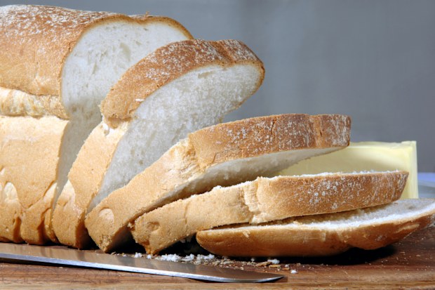 Crusty loaf of finest bread on a bread board with a platter of butter in the background and the knife that sliced it in the foreground. Good sharpness through the image.