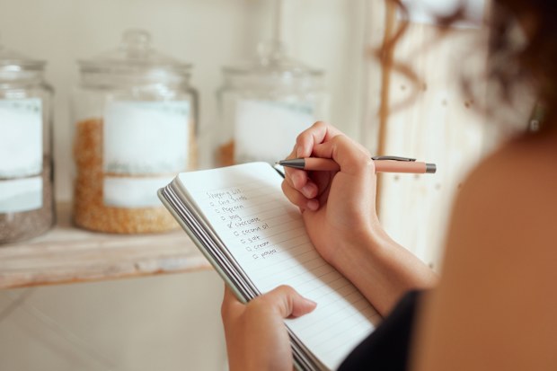 Budget planning, making shopping list and managing household expenses to save money. Financial accountability at home. Woman making shopping list for groceries on a notebook to plan a meal for dinner