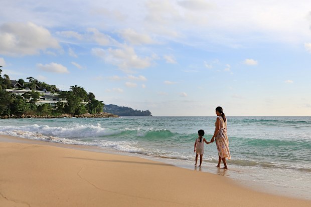 Pregnant mother and daughter walking together on the beach at sunset.