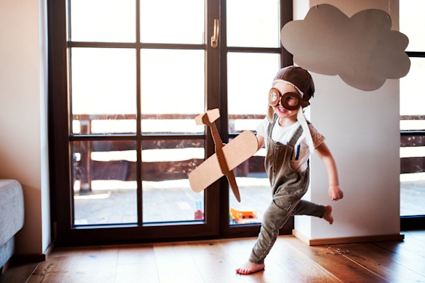 A toddler boy with carton plane and clouds playing indoors at home, flying concept.