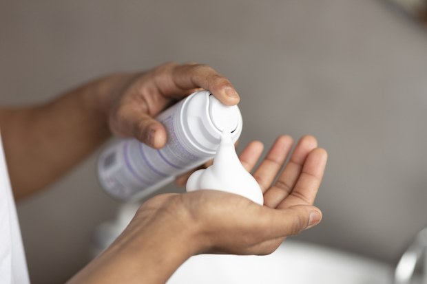 Unrecognizable man applying shave foam on hand, standing in bathroom and preparing for shaving, closeup. 