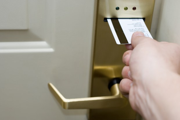Male hand inserting a magnetic strip keycard into a electronic hotel door lock to unlock the door.