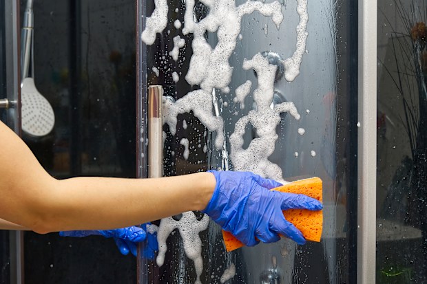 Cleaning of shower steam cabins from Calcium deposits. Cleaning in the bathroom. woman hand in blue gloves with rag and detergent, washing and polishing shower booth from Calcium stone.