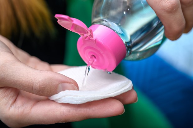 A bottle with micellar fluid for make-up removal and facial care, liquid poured onto a cosmetic pad