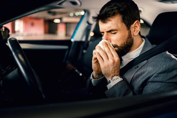 Businessman blowing his nose inside the car