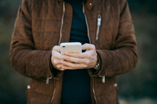 Young man holding smart phone reading text.