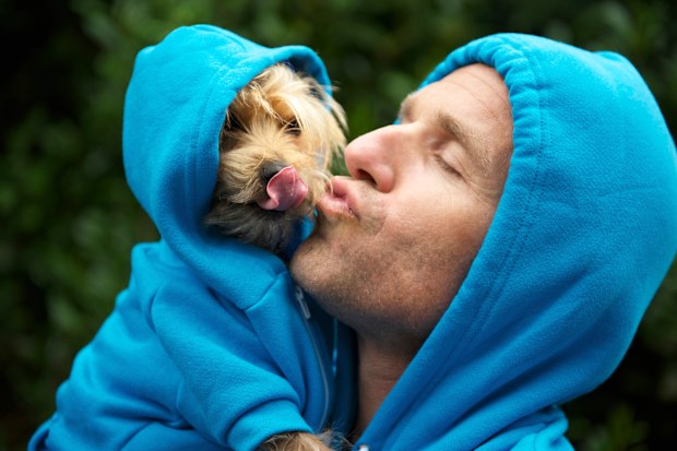 Man kisses his best friend dog in matching blue hoodies in bright green park background outdoors