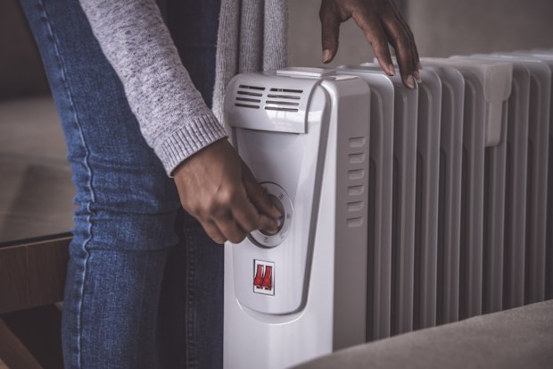 Close up image of female's hand rotating rotary switch to increase / decrease the temperature of an electric heating radiator (action in motion). The woman standing at the domestic room, touching on/off the rotate button.