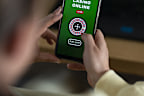 An over the shoulder shot of a young woman sitting at a desk, she is using her smart phone to gamble in an online casino.
