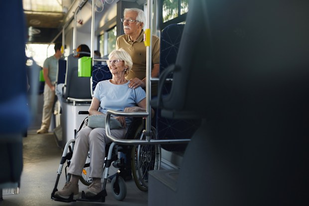 Happy disabled senior woman in a wheelchair and her husband traveling by a bus.