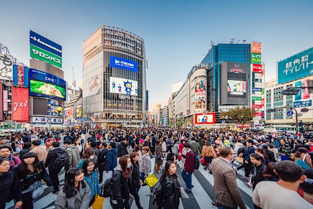 People crossing the crowded famous Shibuya Crossing in Downtown Tokyo, illuminated Shibuya Buildings with billboards in the background. Twilight light, close to sunset. Shibuya Crossing, Shibuya Ward, Tokyo, Japan, Asia.