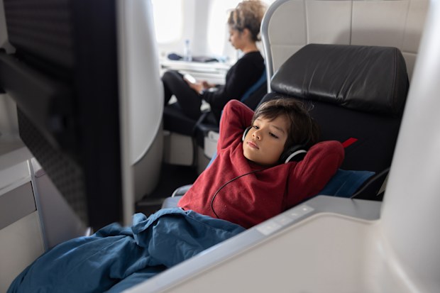 boy traveling by plane in business class and watching a movie using headphones