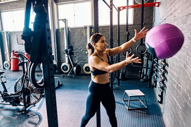 Female athlete throwing a medicine ball against the wall in a gym. Side view of a woman performing strength training exercise in a fitness studio.