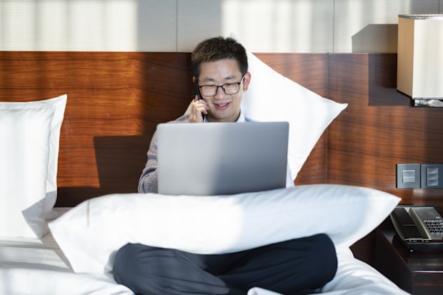 Worker typing on laptop in hotel bed