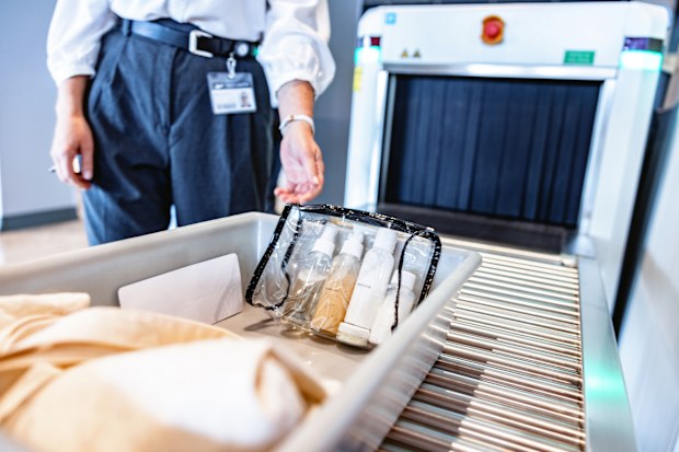Close up shot of a tray filled with liquid toiletries in a clear zip top bag. The tray is on a roller conveyors table and is ready for a x-ray scan.