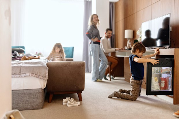 Family unpacking/ packing in hotel room, father is working on laptop, kids are watching cartoons