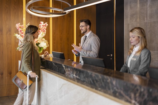 Positive bearded young receptionist standing at the desk and talking with the friendly visitor