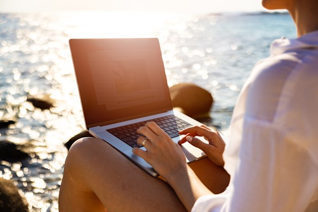 Modern young Caucasian female freelancer, working on laptop, from the rocky beach , during her vacation