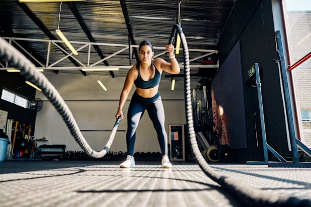 Female athlete performing battle rope exercise in a gym. Front view of a woman doing functional training workout indoors.